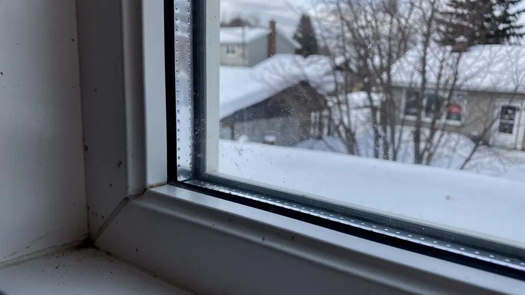 Fenêtre à triple vitrage installée dans une maison canadienne, vue de l'intérieur montrant les multiples couches de verre et le paysage hivernal enneigé à l'extérieur Fenêtre à triple vitrage installée dans une maison canadienne, vue de l'intérieur montrant les multiples couches de verre et le paysage hivernal enneigé à l'extérieur